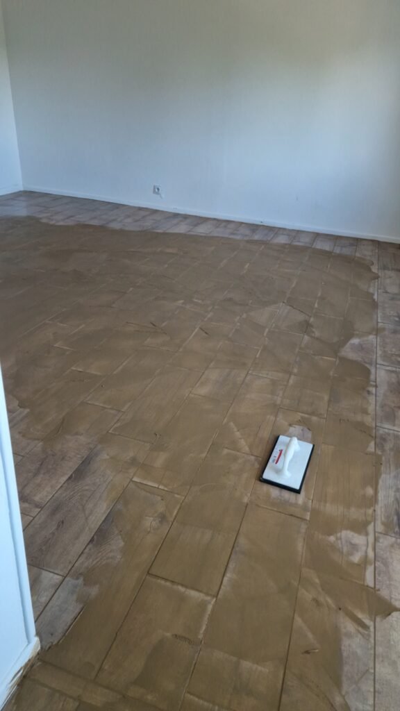 Application des joints couleur hêtre sur un carrelage imitation parquet à Moncy-Notre-Dame.